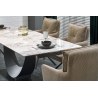 Stół rozkładany z powierzchnią imitującą biały marmur, czarne podstawy, otoczony beżowymi, pikowanymi krzesłami; na stole talerz